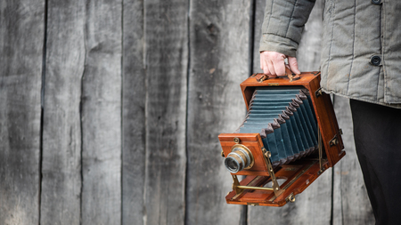 Large format retro camera in photographer hand. Concept - photography of the 1930s-1950s. Retro wooden wall on background, copy space for textの写真素材