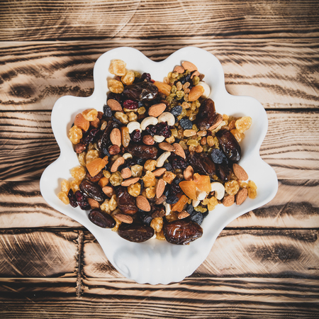 Plate of dried fruits on wooden table, Mix of nuts and berries: cashews, hazelnut, almonds, yellow, brown and blue raisins raisins, cranberries, dried dates and apricotsの写真素材