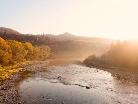 Beautiful autumn morning in picturesque Carpathians. Soft sunlight awakens nature from sleep. Light mist extends over the river.の写真素材