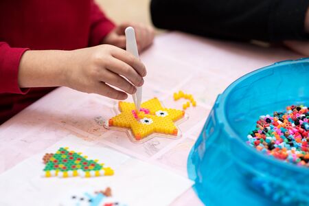 Little girl creates pattern using perler beads. Fusible colorful beads. Toy that develops the imagination and creativity of child. Process close upの写真素材