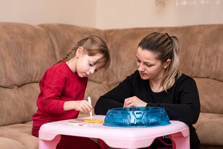 Little girl makes art toy from fusible colorful beads. Mom inspires her daughter. Game at home. Toy that develops the imagination of child, also known as perler beads.の写真素材