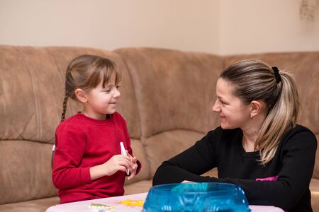 Little caucasian girl has a good time with mom playing the perler beads. Toy that develops the imagination of child. Game at homeの写真素材