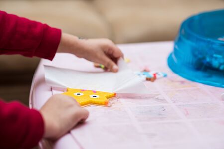 Little girl removes parchment paper from just created toy of fusible colorful beads. Process close-upの写真素材