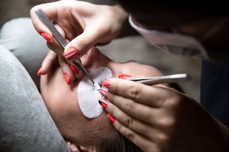 Bunch of artificial eyelashes in tweezers. Extensions of artificial eyelash, process close Woman in a beauty salon. Beauty and self-care.の写真素材