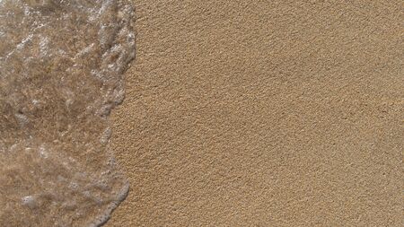 Soft sea wave covers the sand on the shore of sandy beach, top view, close up. Summer horizontal background with copy spaceの写真素材