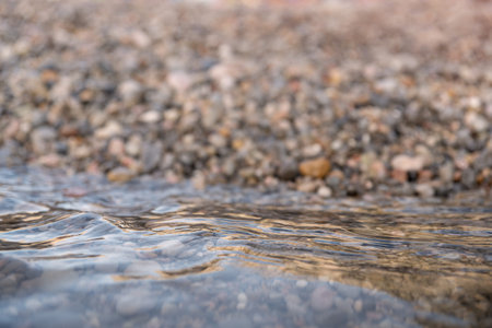 Transparent seawater covers the sea pebbles, sunset time on the seashore. Natural summer background...