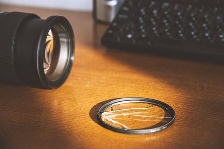 Broken glass of UV filter near the DSLR camera on the photographer work table. Sample of a crushed filter and a saved lens. Theme of protecting an expensive lens from damage. Matte effect.の写真素材