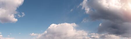 Blue cloudy sky background with warm sunny tonings. Wide-angle panoramic natural background, banner format.の写真素材
