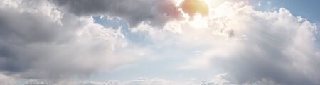 Beautiful cloudscape with warm sunny tonings. Blue sky covered with clouds. Warm sunlight and sun rays pass through the clouds and illuminate them. Ultra-wide panoramic natural background.の写真素材