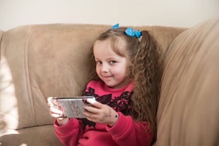 Pretty child is smiling and holds cellphone in handsの写真素材