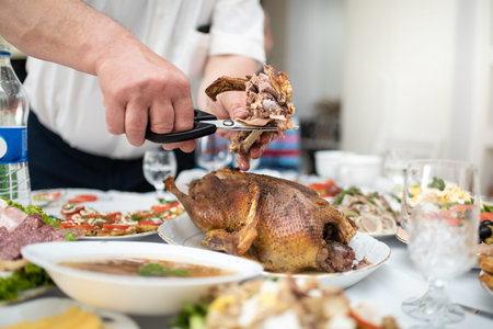 Man divides with scissors freshly baked duck into portions, process close up. Events take place at home during a family meeting to celebrate the solemn event. Foods and dishes on a tableの写真素材