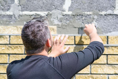 Man decorates the facade of the fence with decorative torn bricks. Work at home during quarantine. Do it yourself.の写真素材