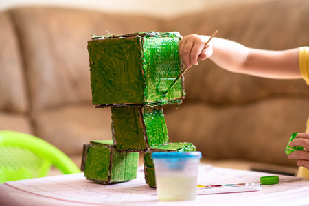 Child paints a paper handicraft toy in green color. Home leisure and self-development.