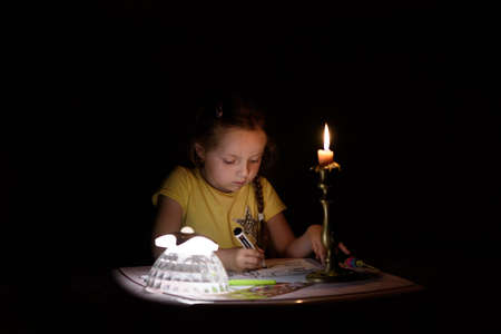 Little girl draws fantasy characters near candle in a dark room. Child doing favorite thing during a power outage.の写真素材