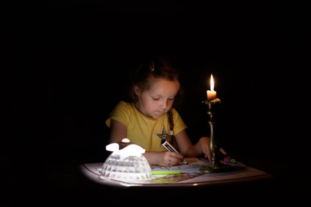 Little girl draws fantasy characters near candle in a dark room. Child doing favorite thing during a...