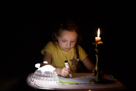 Little girl draws fantasy characters near candle in a dark room. Child doing favorite thing during a power outage.の写真素材