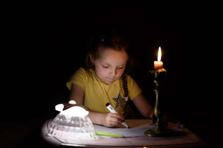 Little girl draws fantasy characters near candle in a dark room. Child doing favorite thing during a power outage.の写真素材