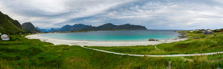 Panorama of Rambergstrand beach on the Lofoten islands in cloudy weather. Mountains, sandy beach, grass and azure water. Norway sea.の写真素材