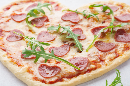 Close-up shot of heart shaped pizza with pepperoni, mozzarella and arugula. Valentine's Day romantic food concept.の写真素材