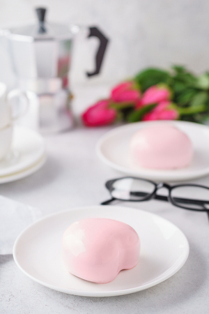 Trendy mousse cakes with pink mirror glaze. Heart shaped treats for Valentine's day. Flowers in the background.の写真素材