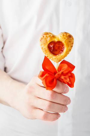 Man in a white shirt giving a heart shaped pie pops on a stick decorated with red bow. Valentine's Day gift concept.の写真素材