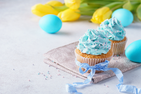 Decorated cupcakes with cream, blue eggs and yellow tulips. Easter dessert concept. Space for text.の写真素材