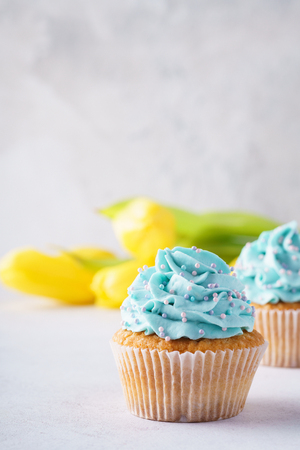 Vanilla cupcakes with blue frosting and yellow flowers in the background. Mothers Day or Birthday dessert.の写真素材