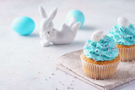 Easter vanilla cupcakes with cream cheese frosting and candy eggs. Cute bunny in the background.の写真素材