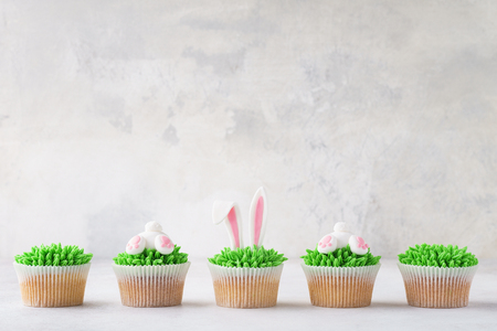 Homemade Easter cupcakes in a row. Decorated as grass, bunny butt and bunny ears.の写真素材