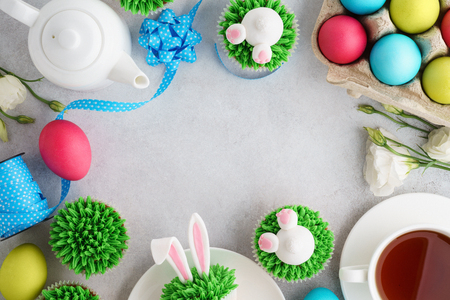 Easter frame background with bunny cupcakes, tea and painted eggs. Top view, copy space.の写真素材