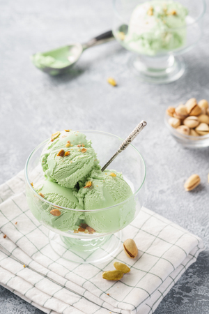 Pistachio ice cream in a bowl with chopped nuts on a grey background. Summer dessert concept.の写真素材