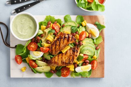 Healthy cobb salad with grilled chicken, avocado, tomato, eggs, beans and corn on marble serving board.の写真素材