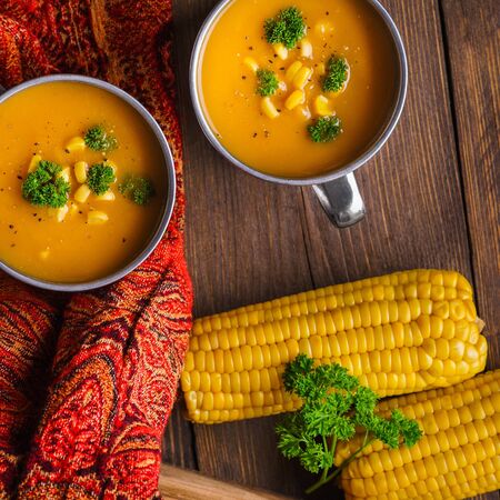Pumpkin soup served with corn and parsley on a dark wooden background with red napkin.の写真素材