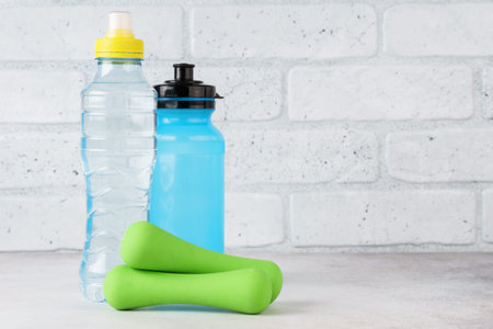 Water bottles and dumbbells on light background. Fitness, sport and health concept. Copy space.