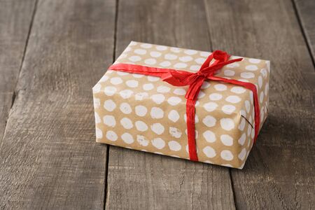 Paper wrapped gift box decorated with red bow and ribbon on wooden background. Copy space.の写真素材
