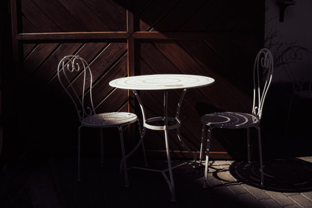 Artistic composition of a small wrought iron table and two chairs casting decorative shadows on a...