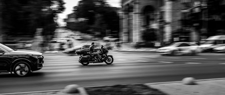 Kyiv, Ukraine - July 2024: A motorcyclist rides through a city intersection, captured in motion blur among cars and pedestrians. Black and white urban street scene. Editorial use only.のeditorial素材