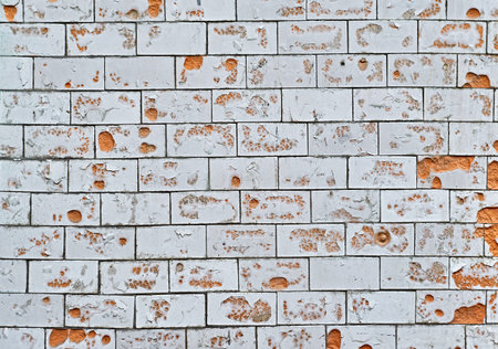 The texture of an old white, tiled wall with broken, cracked wall tiles. Background.