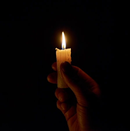 A hand holding a lighted candle in the dark. The light of a burning candle in a dark room. A candle on a black background.の写真素材