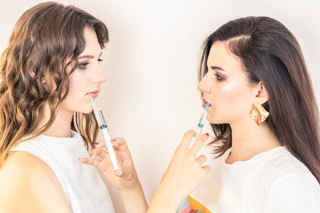 Two beautiful girl holding syringes. The concept of cosmetic services, skin care, modern fashion