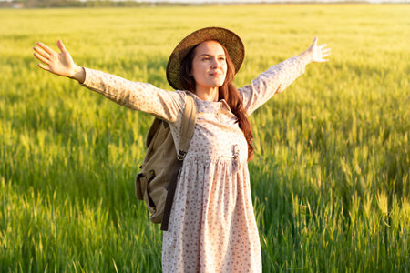 Traveler with a backpack in a field of wheat at sunset. Woman outdoor in nature at the backdrop of...