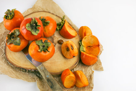 Persimmon lies on a wooden Board on a white background. Persimmon close - up whole and cut into...