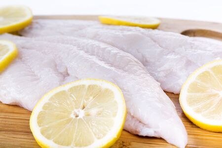 Fresh catfish fillets on a cutting board with lemon and isolated on white.の写真素材