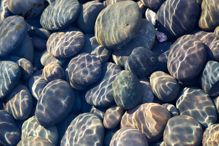 Multicolored pebbles and cobblestones in a stream with sunlight diffraction patterns from surface...