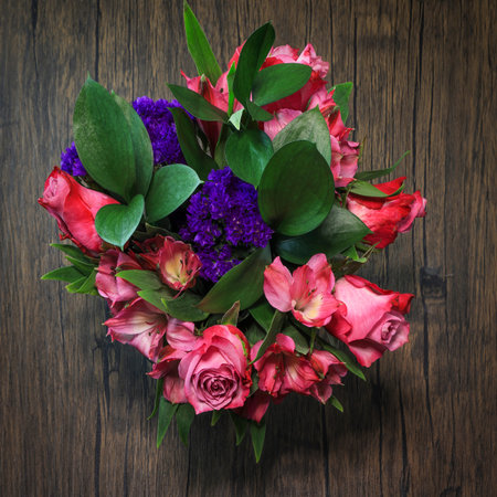 Bouquet of red roses and purple violets photographed from above on a wooden table.