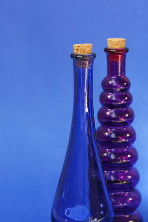 Empty blue and purple glass bottle with corks in the tops. Shot against a blue backgroundの写真素材