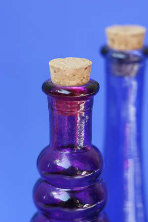 Empty blue and purple glass bottle with corks in the tops. Shot against a blue backgroundの写真素材