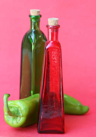 Glass bottle with a cork in the top and a large pepper in between. Shot against a red backgroundの写真素材