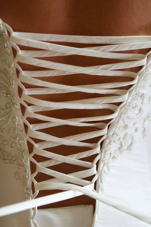 A young woman has her white dress laced up from the back.