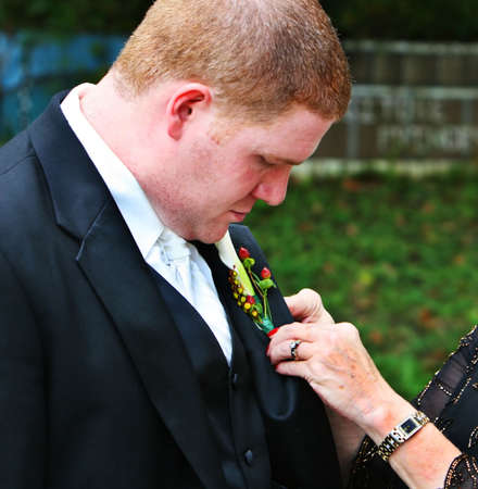 A mother pins a boutonniere on her sons jacket before the wedding ceremonyの写真素材